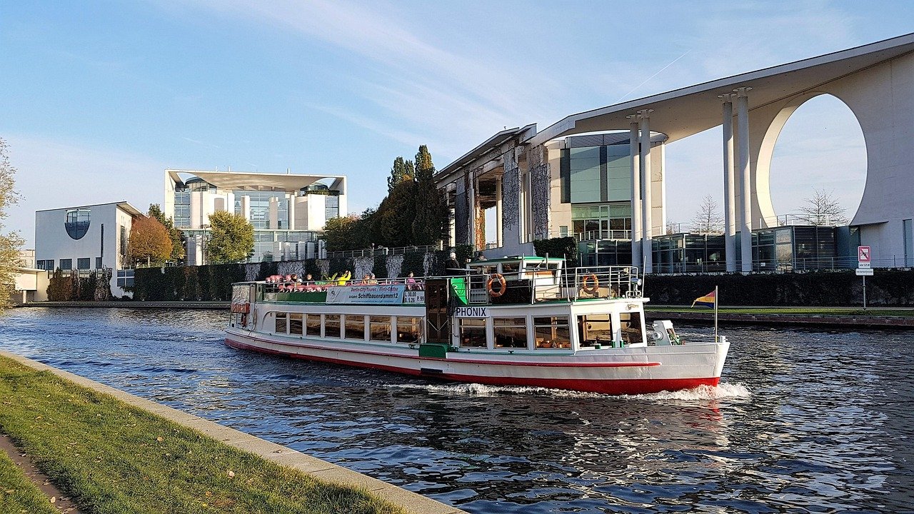 Turistbåt som kryssar på floden med moderna regeringsbyggnader och klar himmel i bakgrunden