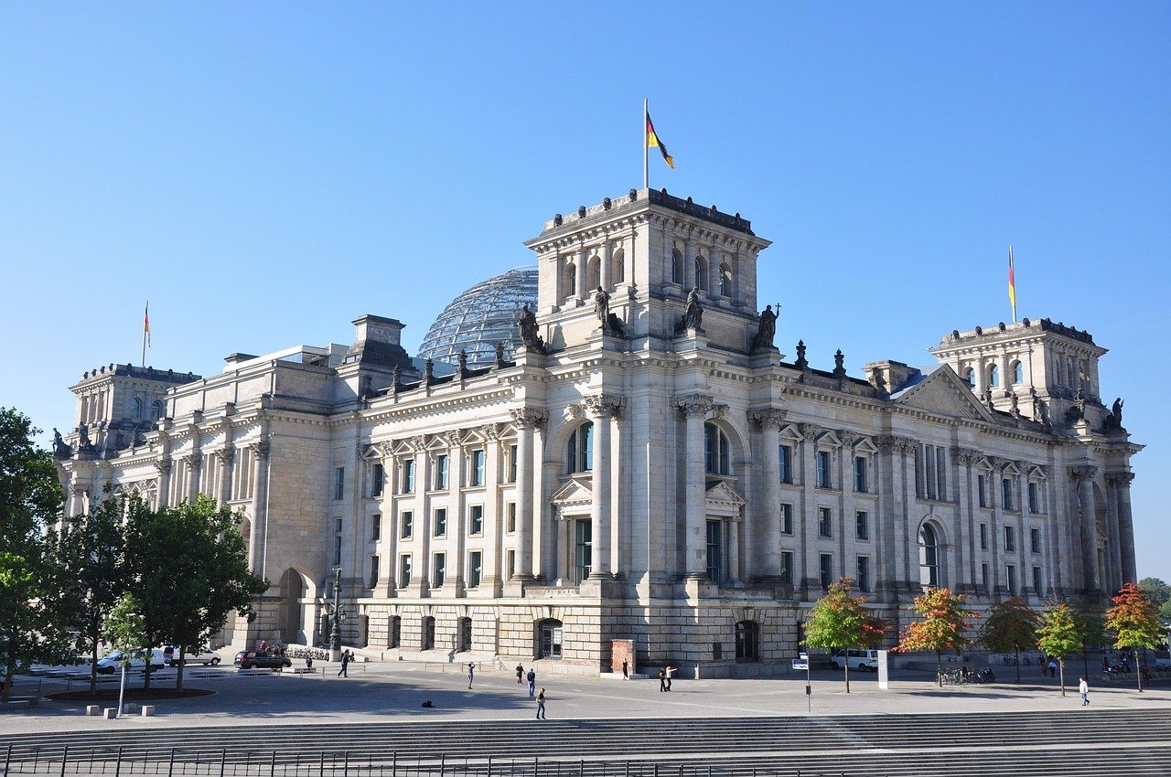 Historiska riksdagsbyggnaden i Berlin med tyska flaggor och glaskupol under klarblå himmel