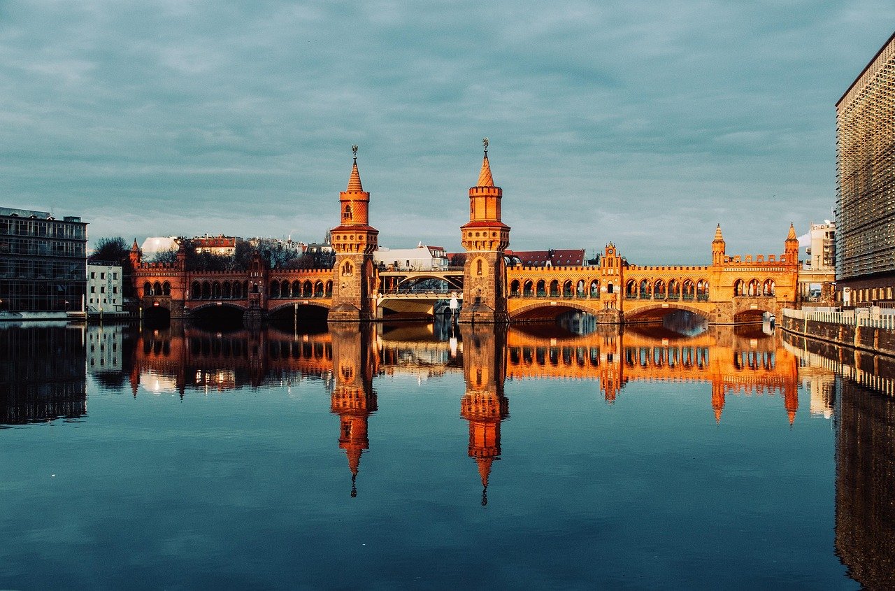 Oberbaumbron i Berlin reflekterad i lugnt flodvatten under molnig himmel under dagtid