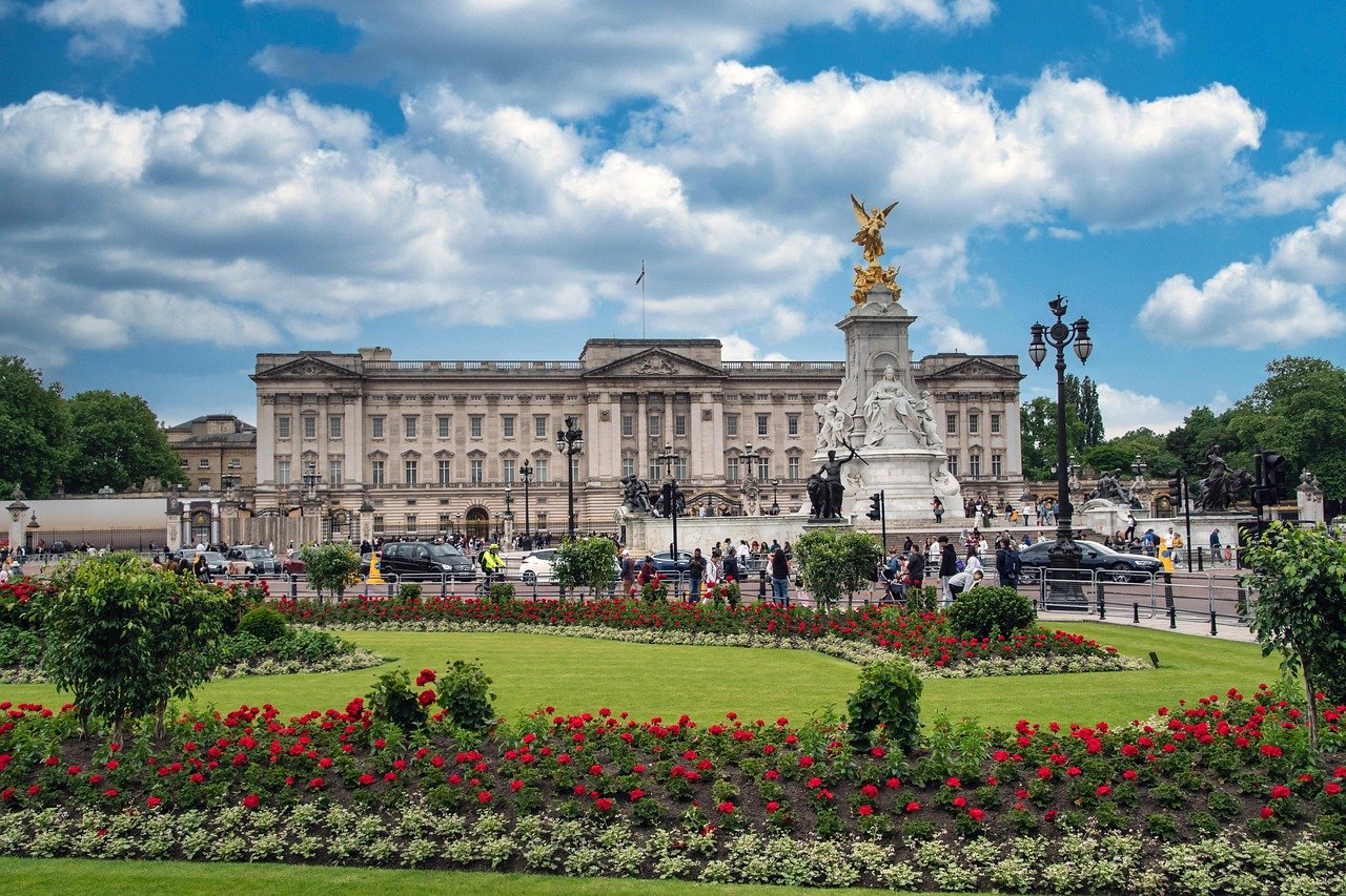 Buckingham Palace i London med Victoria Memorial och livlig blomsterträdgård under en delvis molnig himmel