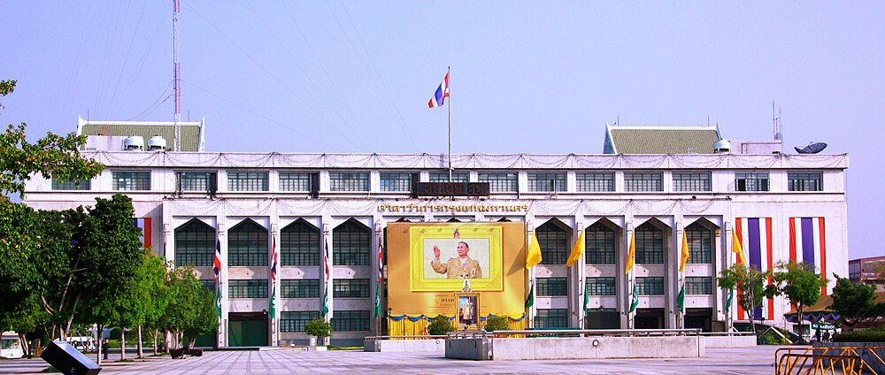 Thailändsk regeringsbyggnad med kungens porträtt och flaggor Regeringsbyggnad i Thailand med stor porträtt av thailändska kungen och nationella flaggor som visas framträdande