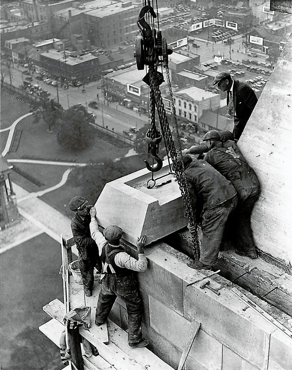 Byggnadsarbetare installerar stenblock på skyskrapa Historiskt svartvitt foto av byggnadsarbetare som installerar stora stenblock på en höghusfasad