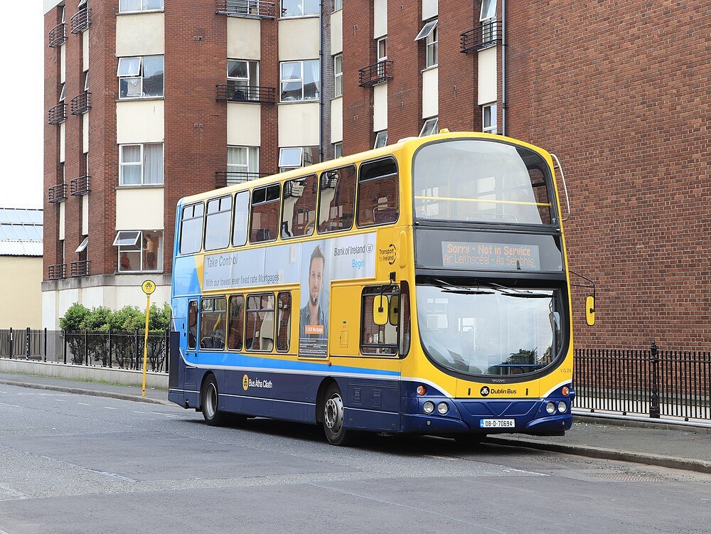 Dubbeldeckare Dublin-buss parkerad på stadsgata med tegelbyggnader och reklam på sidopanel