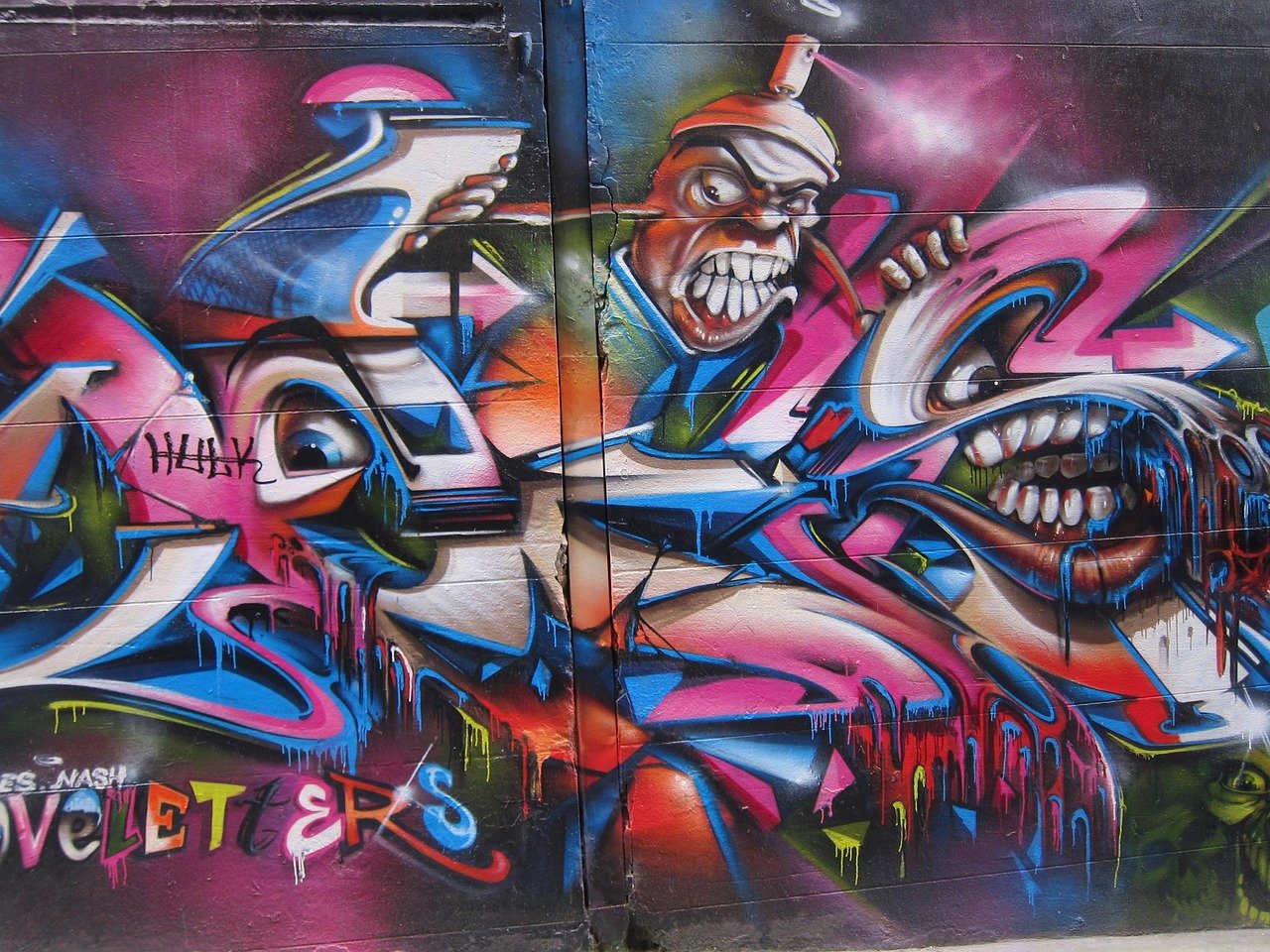 Färgglad graffiti på vägg med abstrakta ansikten med överdrivna tänder och livliga droppande färgeffekter