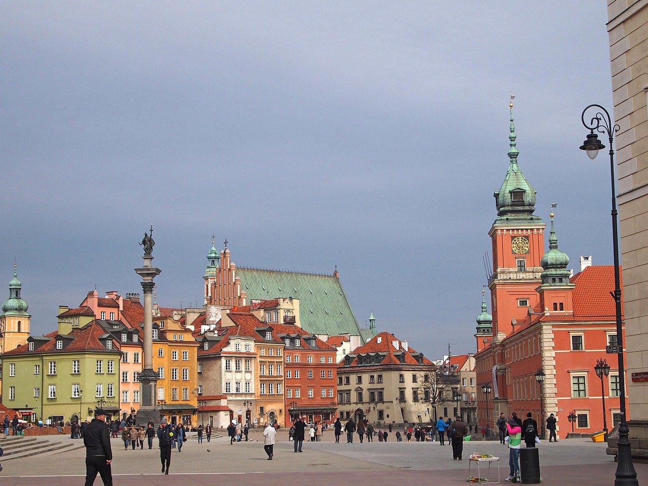 Färgglada historiska byggnader och ett klocktorn på det gamla torget i Warszawa, Polen med människor som promenerar runt.