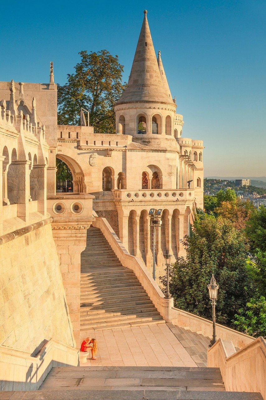 Fiskarbastionen i Budapest med sten trappor och en person som sitter, historisk arkitektur under klarblå himmel