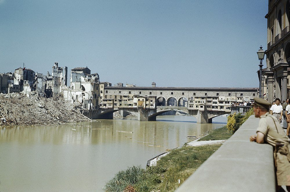 Ponte Vecchio-bron och Krigsskadade Byggnader Florens Historiska Ponte Vecchio-bron över Arno-floden med skadade byggnader och bråte på flodbanken i Florens, Italien