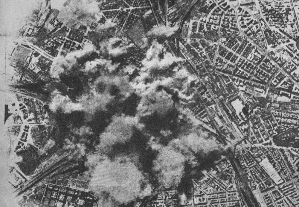 Flygvy av krigstida urban explosion och rök Flygfoto i svartvitt som visar en stor explosion och rök över ett stadsområde under krigstida bombning.
