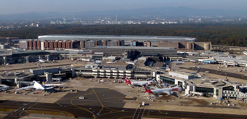 Flygfoto av en livlig internationell flygplats med flera flygplan parkerade vid gater och terminalbyggnader synliga