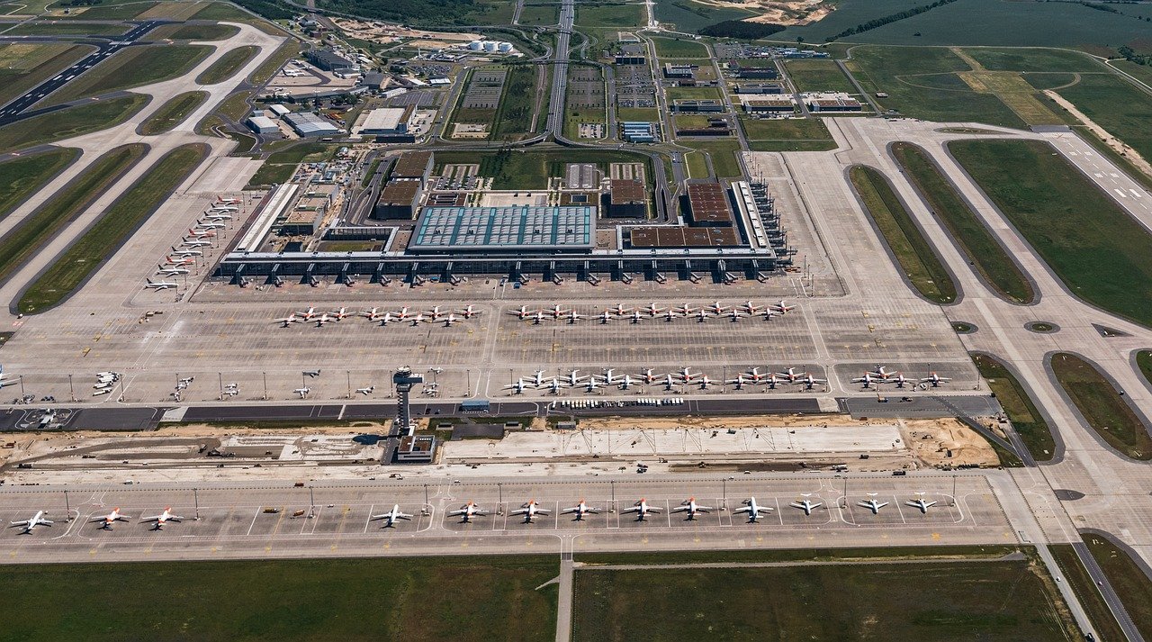 Flygfoto av en stor internationell flygplats med flera flygplan parkerade vid terminaler och landningsbanor synliga