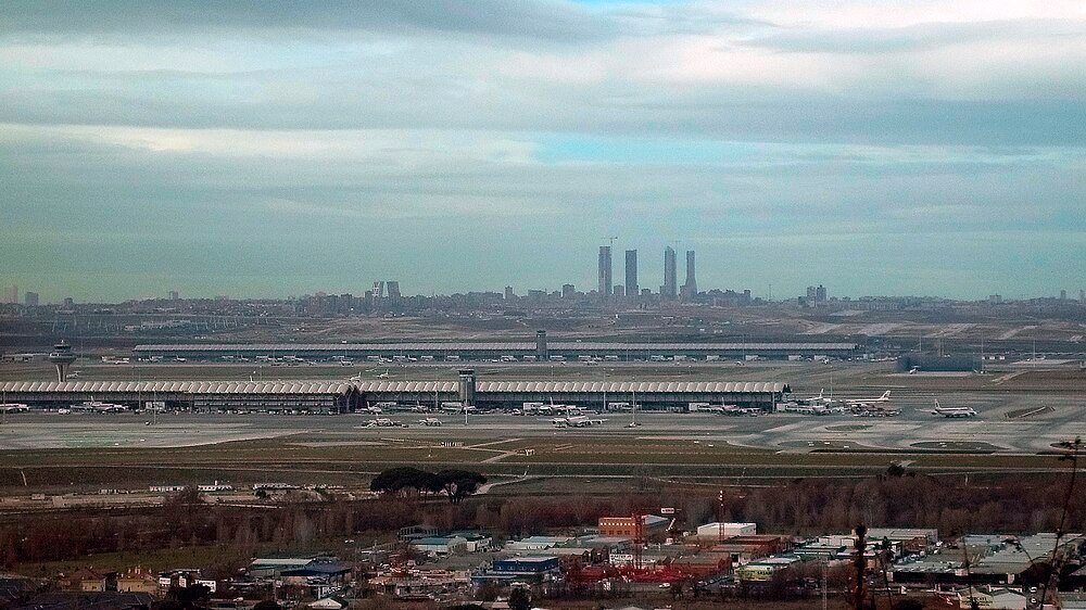 Flygfoto av internationell flygplats med flygplan Flygfoto av en stor internationell flygplats med flera flygplan och terminalbyggnader under en molnig himmel