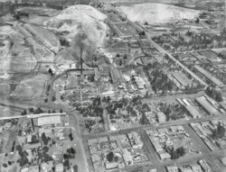 Flygfoto av industriell stad med fabriker och hem Flygfoto i svartvitt av en industriell stad med fabriker, bostadshus och omgivande kullar.