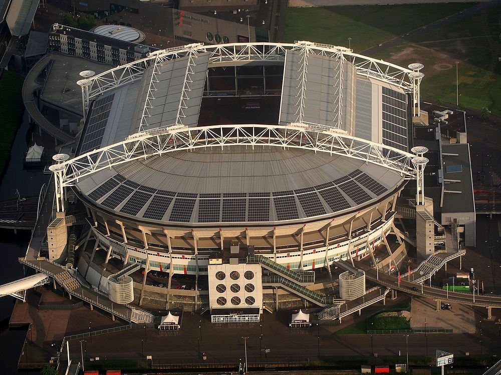 Flygfoto av en stor modern stadion med delvis öppet tak och solpaneler på takstrukturen
