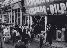 Vintage biografingång med folkmassa samlad utanför Svartvitt foto av en folkmassa samlad utanför en vintage biografingång med skyltar och affischer