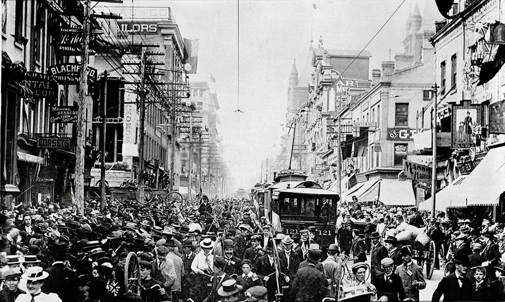 Trång stadsgata tidigt 1900-tal med spårvagnar Historiskt svartvitt foto av en trång stadsgata med tidiga 1900-talets spårvagnar och fotgängare