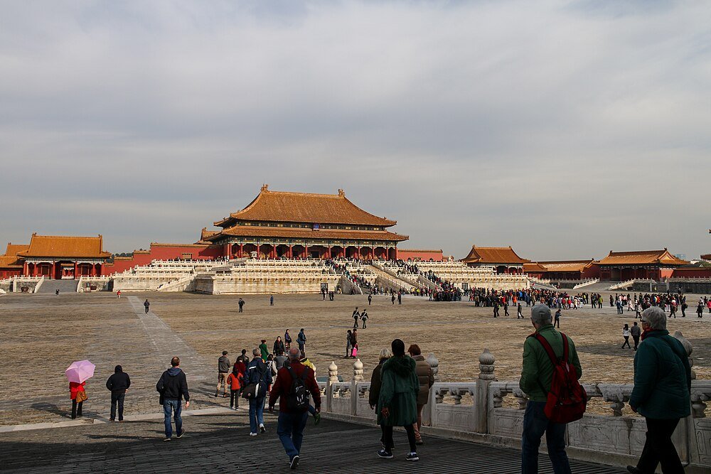 Turister som går mot den förbjudna staden i Peking, Kina, med traditionell kinesisk arkitektur och molnig himmel