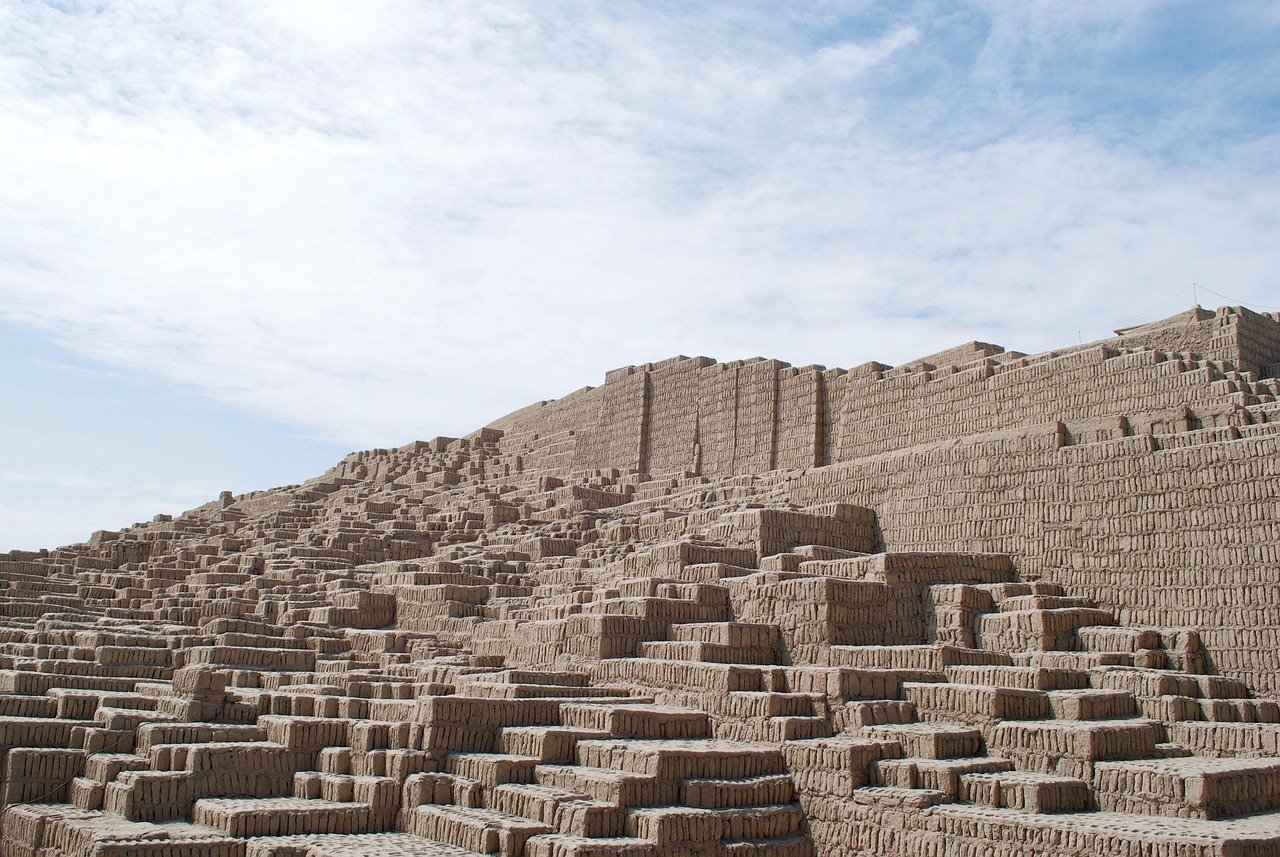 Antika adobepyramidruiner under en delvis molnig himmel, som visar upp trappstegsarkitektur och historisk betydelse