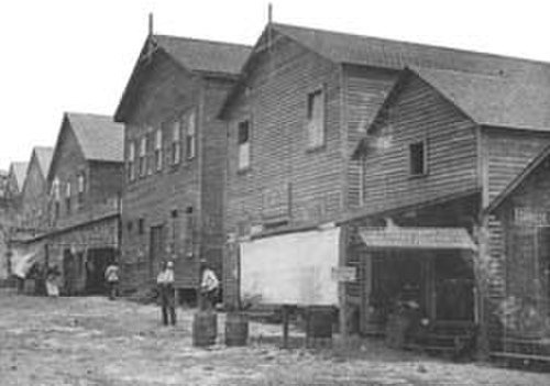 Tidigt 1900-talets träindustriella lager Historiskt svartvitt foto av gamla träindustriella lager med arbetare utanför i början av 1900-talet