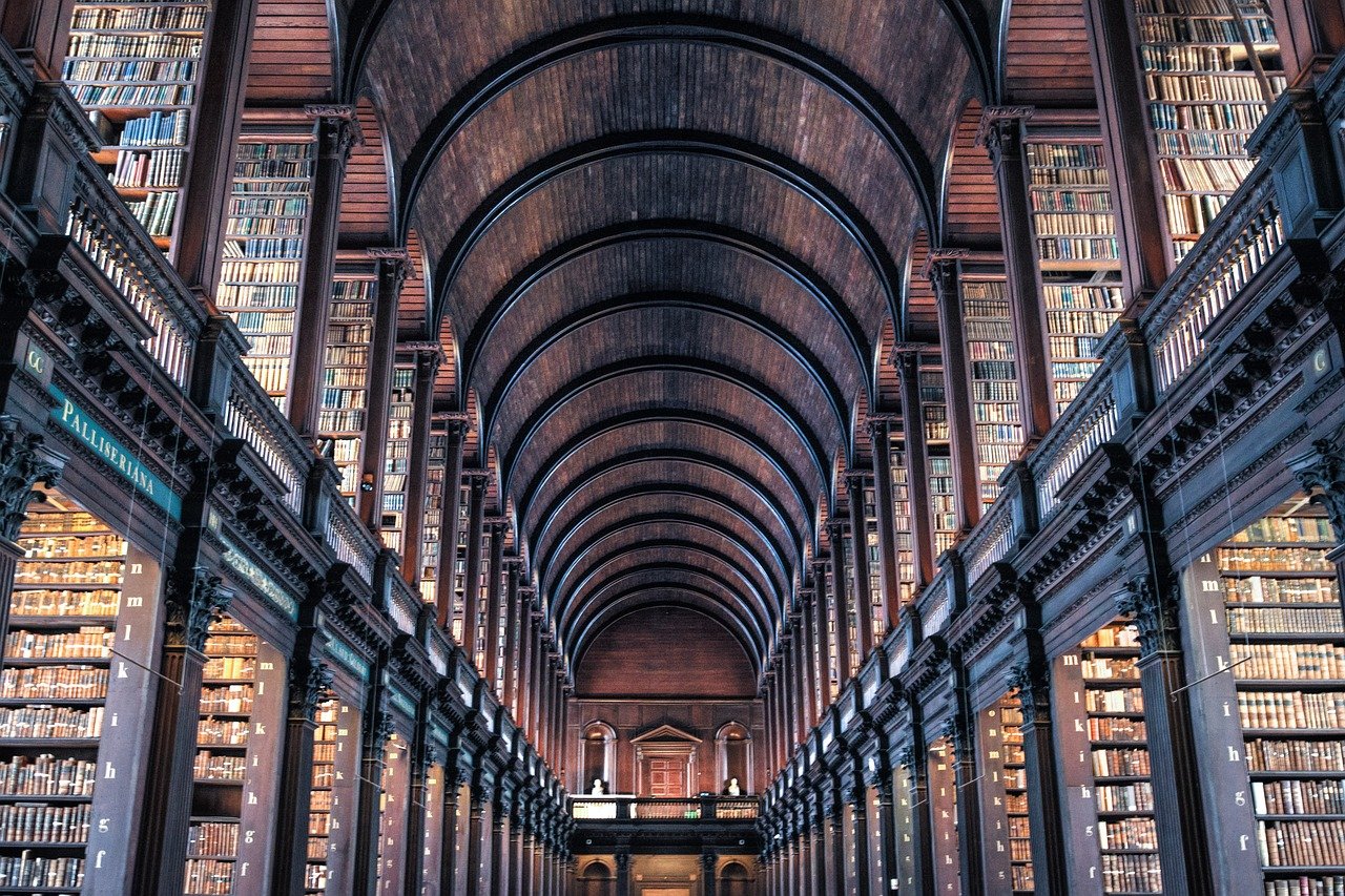 Interiörvy av ett storslaget historiskt bibliotek med höga träbokhyllor och välvt tak fyllt med gamla böcker