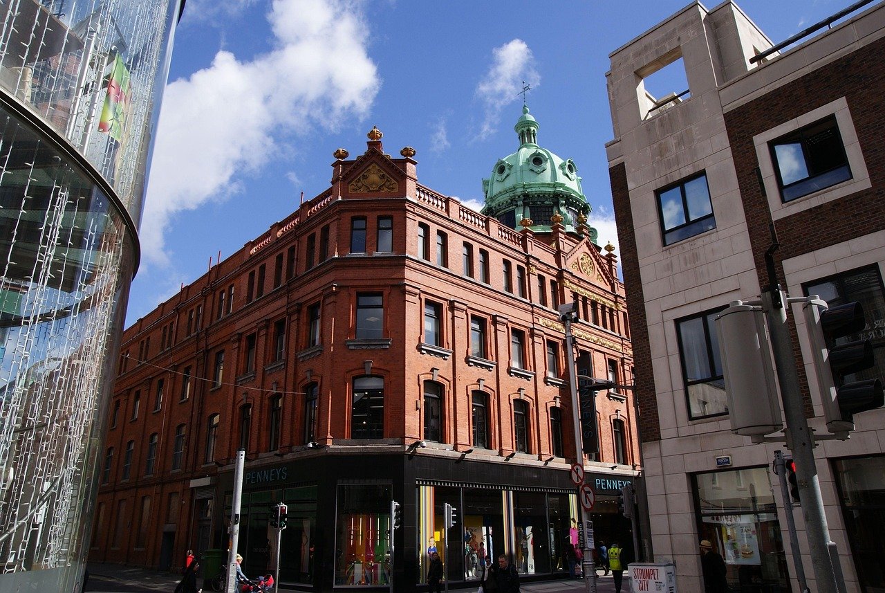 Historisk röd tegelbyggnad med grön kupol och Penneys butik på en solig dag på en livlig stadsgata