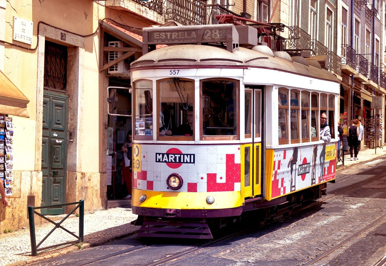 Gul och vit vintage spårvagn nummer 28 med Martini-reklam som reser på kullerstensgata i Lissabon, Portugal