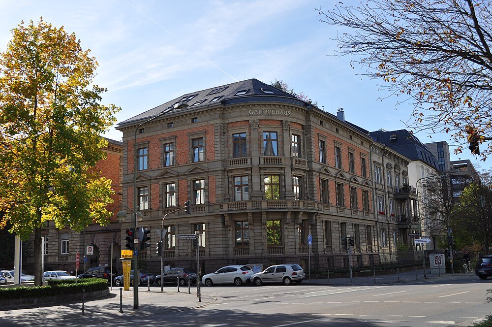 Historisk Galeriehaus-byggnad med klassisk arkitektur och parkerade bilar på en solig dag i en urban miljö