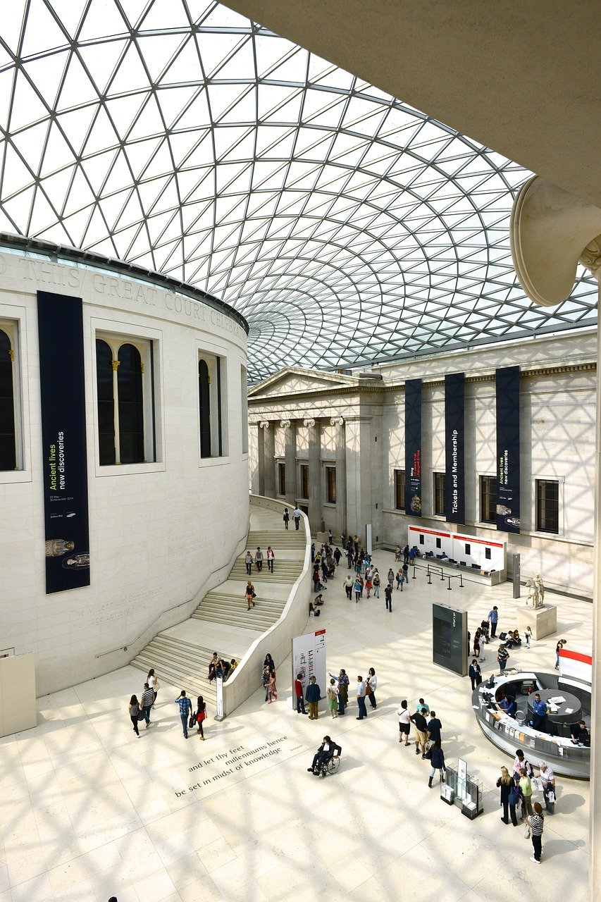 Interiör vy av British Museum Great Court med glastak och besökare som utforskar utställningar och informationsdiskar