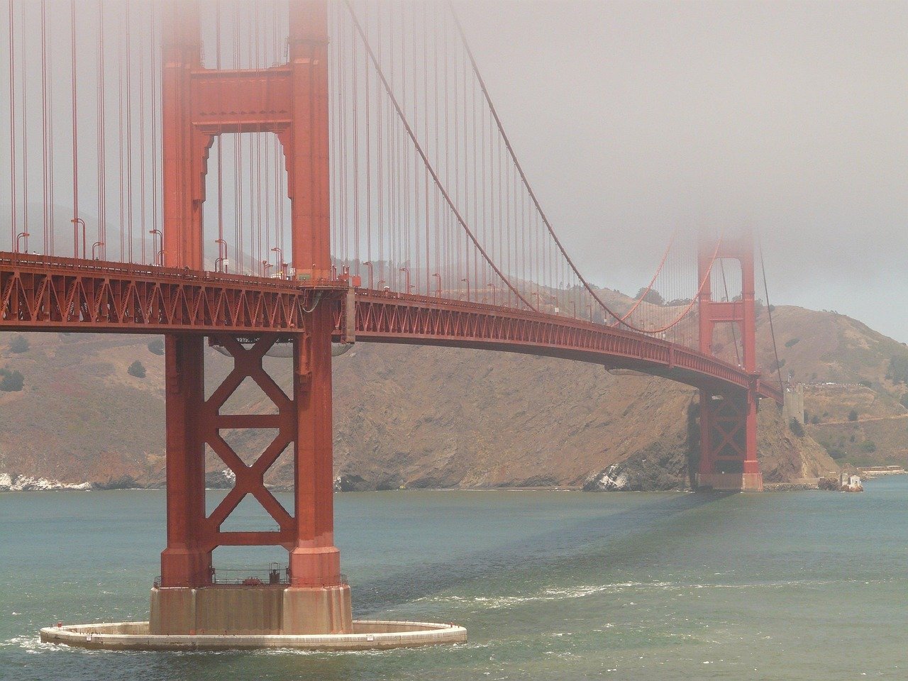 Golden Gate-bron i San Francisco delvis täckt av dimma över bukten med kullar i bakgrunden
