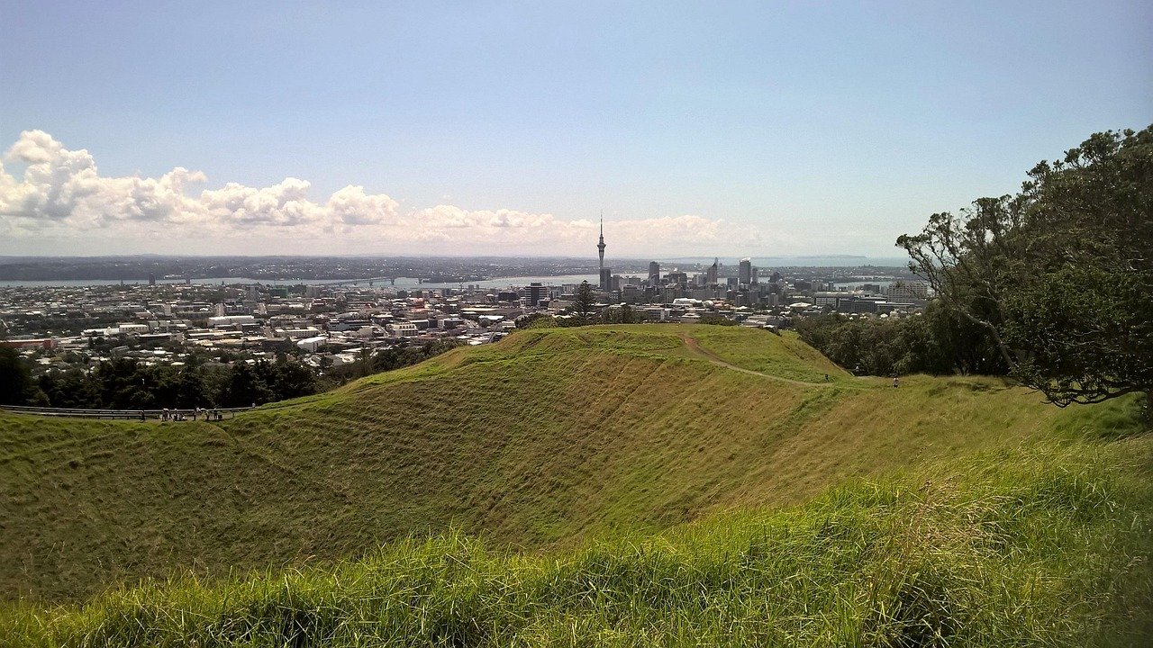 En panoramavy över Aucklands stadssilhuett med Sky Tower från en gräsbevuxen vulkankrater på en klar solig dag