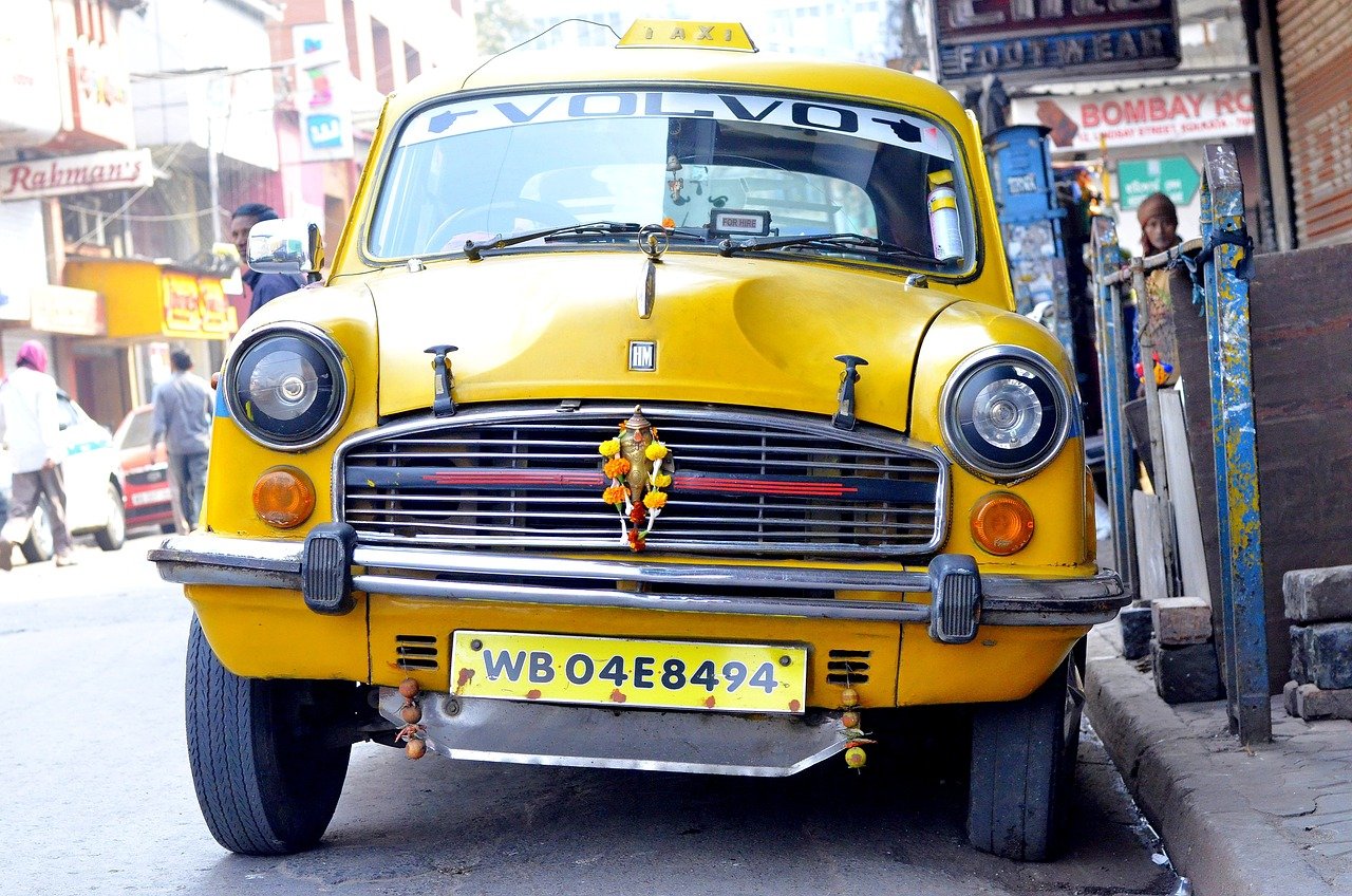 Gul vintage taxibil med registreringsnummer WB04E8494 parkerad på gata i livligt stadsområde