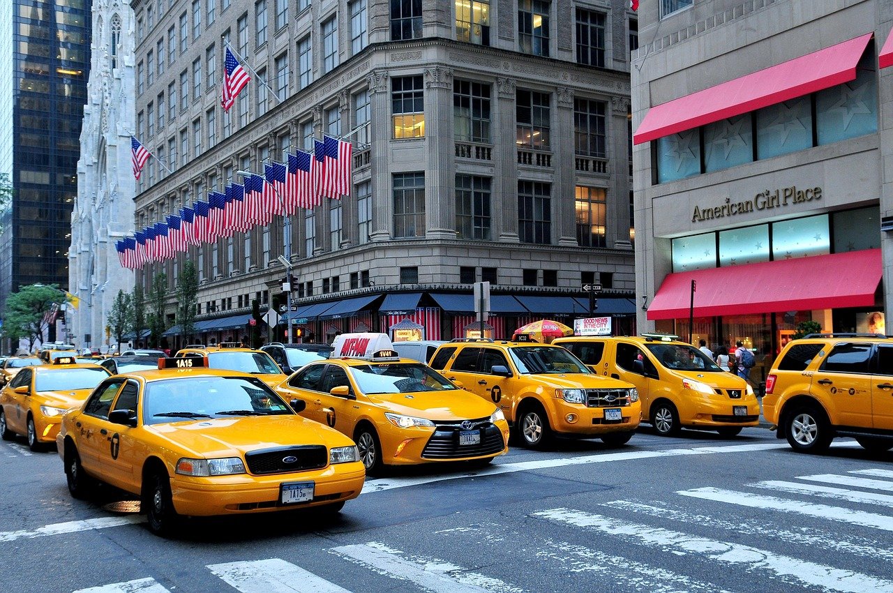 Gula New York City-taxibilar uppradade på en livlig gata med amerikanska flaggor och höga byggnader i bakgrunden
