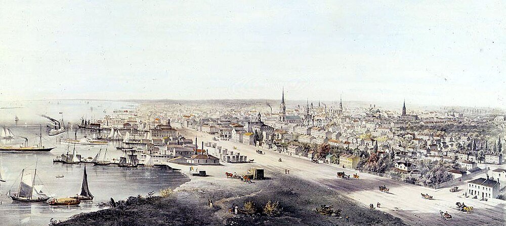 Historisk kuststad med fartyg och strandlinjebyggnader Panoramavy av en historisk kuststad med många segelfartyg, ångbåtar och gamla byggnader längs strandlinjen.