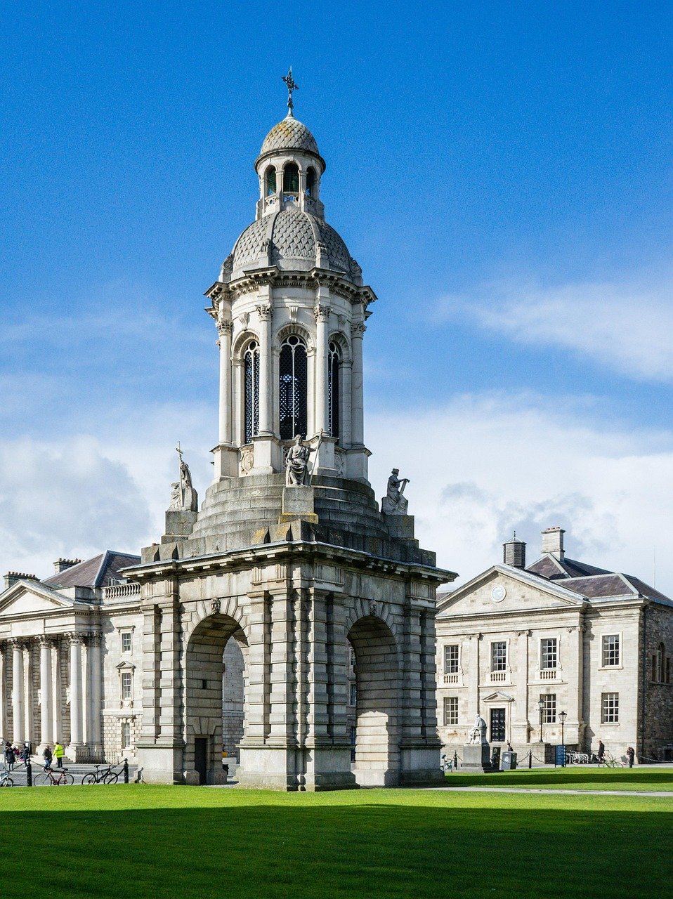 Historiskt stenklocktorn med statyer och valv på Trinity College Dublins campus under blå himmel
