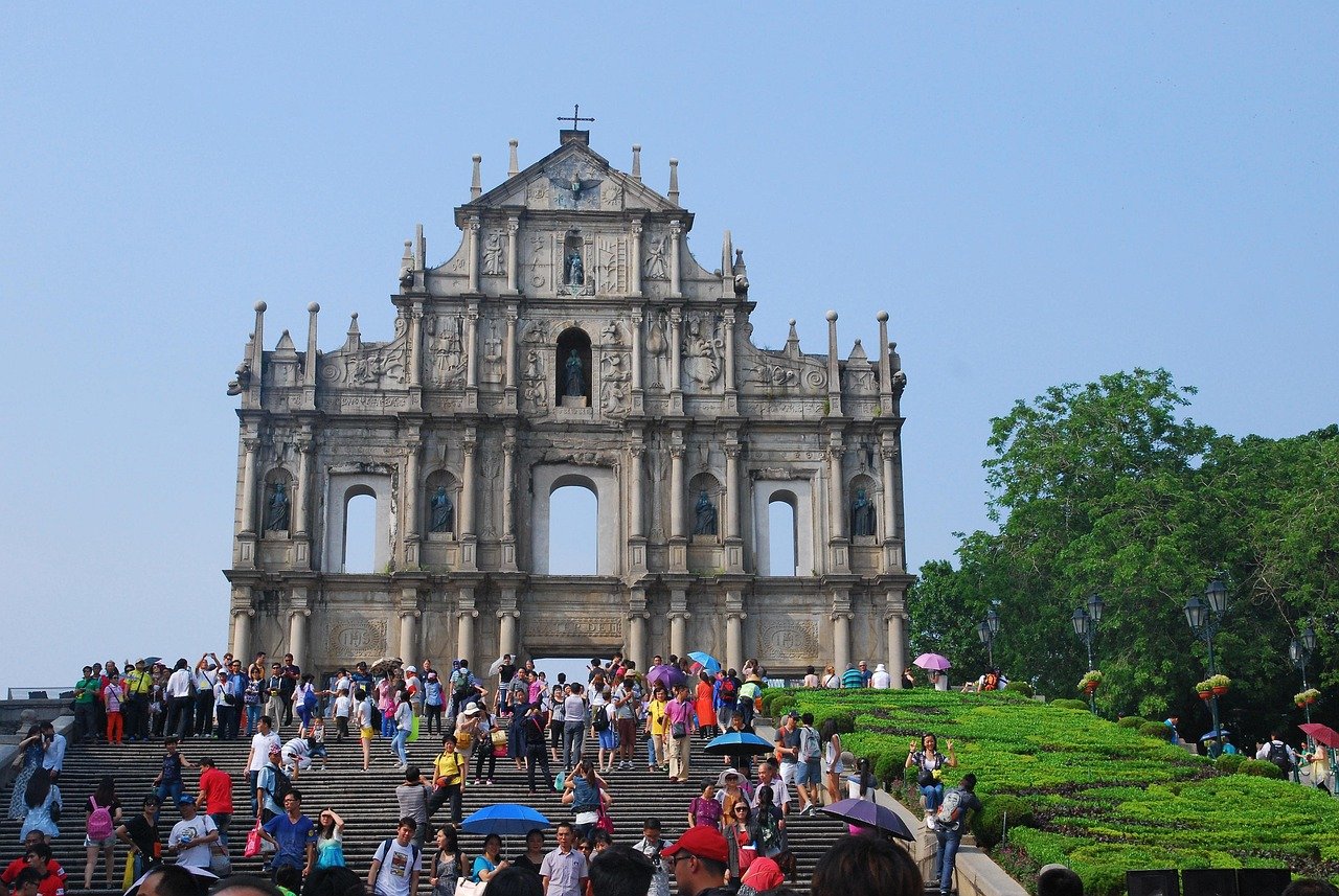 Ruinerna av St. Pauls fasad med turister i Macau Ruinerna av St. Pauls historiska stenfasad med turister och grönska under klarblå himmel i Macau