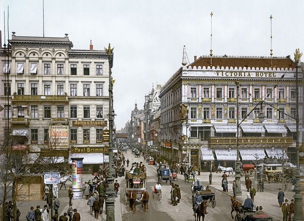 Tidigt 1900-talets stadsgata med Victoria Hotel Historisk stadsgatuscen med hästdragna vagnar, fotgängare och Victoria Hotel-byggnad i tidigt 1900-talets Europa
