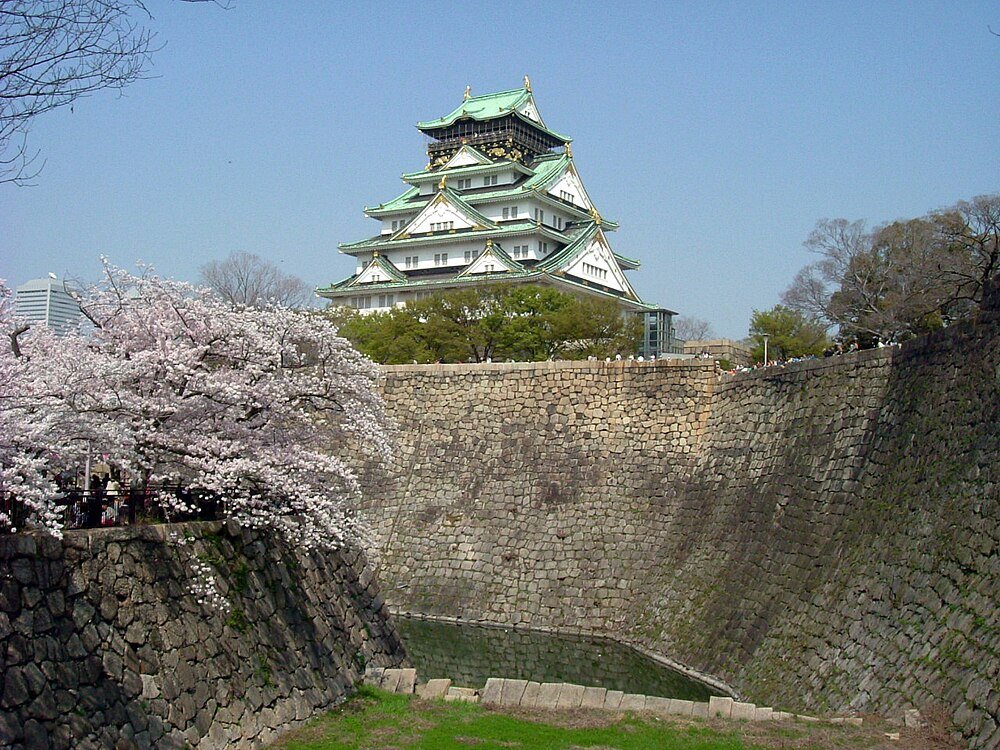 Osaka slott med körsbärsblommor Osaka slott omgivet av körsbärsblomsträd och stenmur under en klarblå himmel i Japan