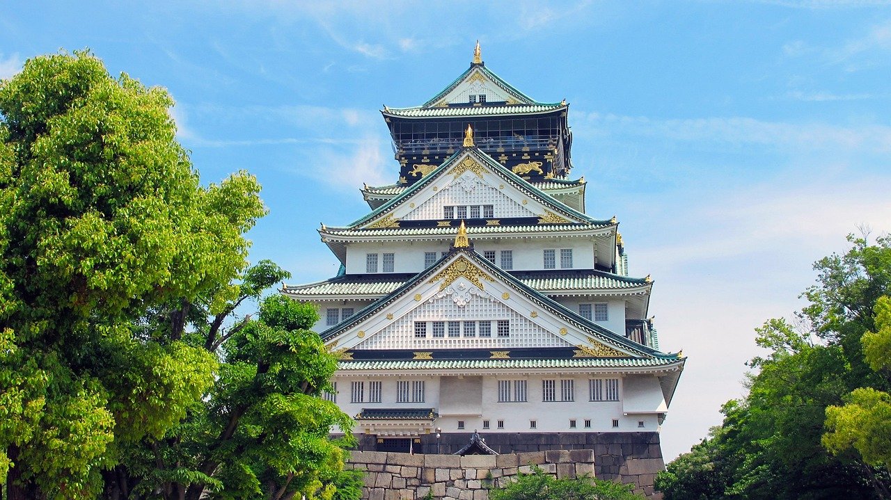 Osaka slott i Japan omgivet av gröna träd under en klarblå himmel, som visar traditionell japansk arkitektur