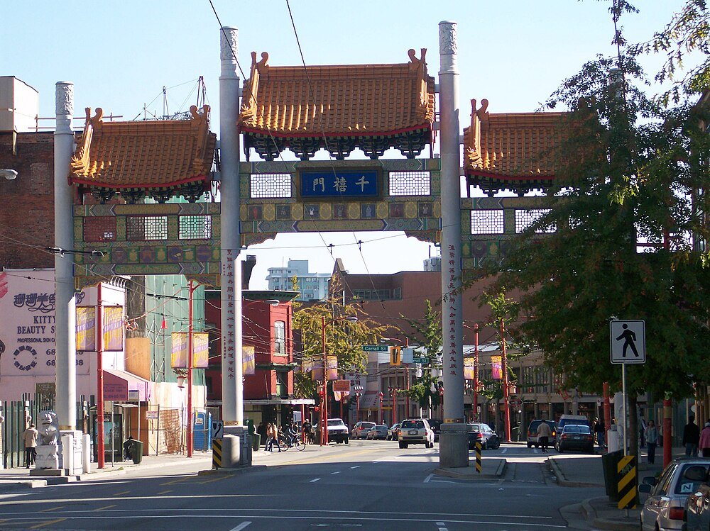 Kinesisk Bågport i Chinatown-distriktet Traditionell kinesisk bågport i ett livligt urbant Chinatown-distrikt med bilar och fotgängare på gatan