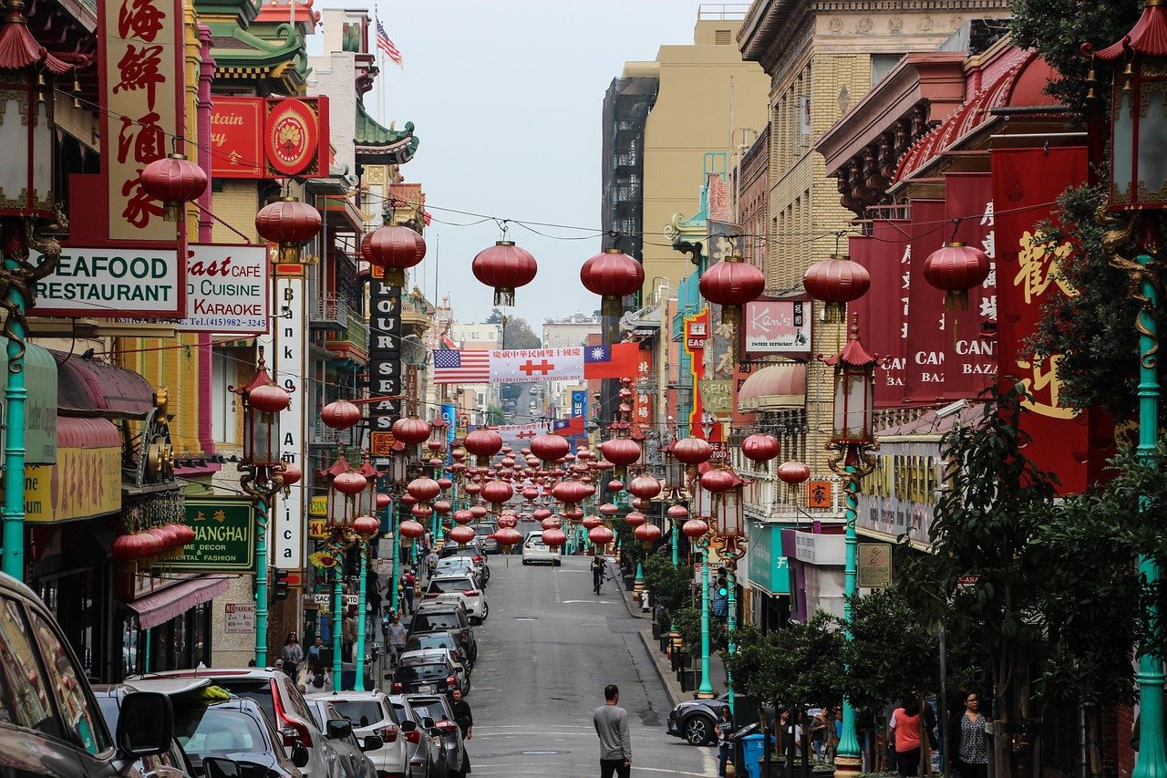 Livlig Chinatown-gata med röda lyktor, asiatiska restauranger och parkerade bilar i en urban stadsmiljö.