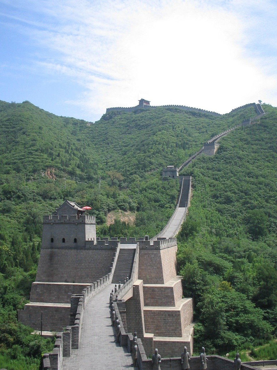 Den Stora Muren i Kina som slingrar sig över gröna kullar under en blå himmel, som visar upp gammal stenarkitektur och vakttorn.