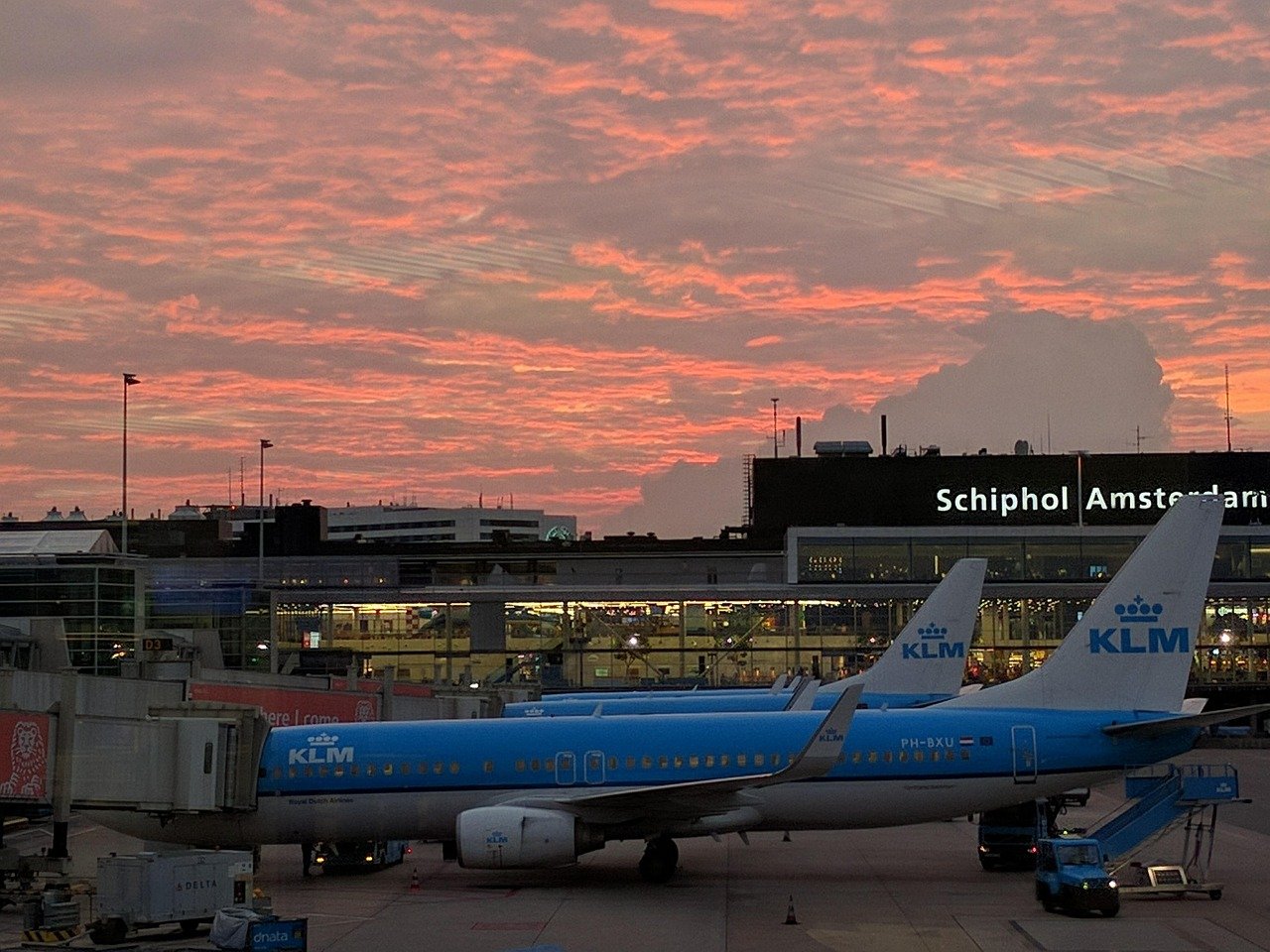 KLM-flygplan parkerade på Schiphol flygplats under en livlig solnedgång med orange och rosa moln på himlen