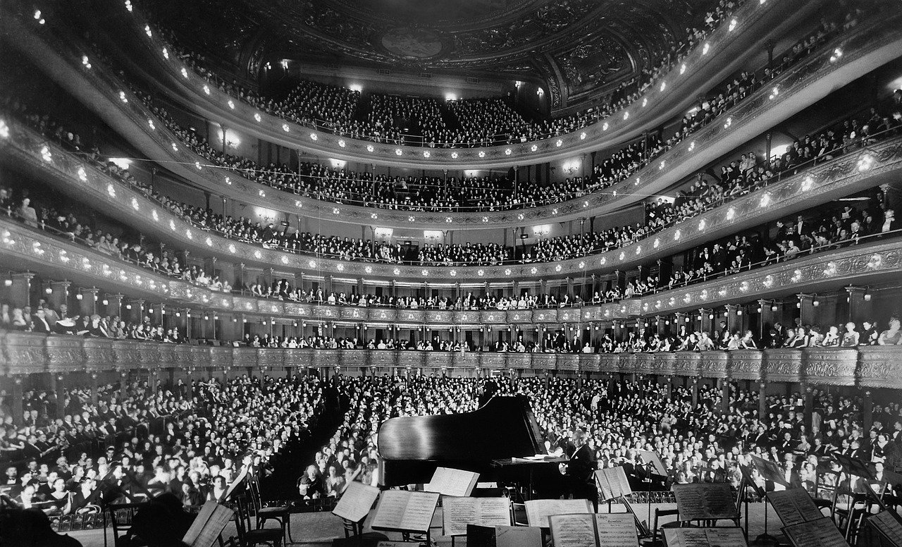 Stor publik i en storslagen historisk konserthall som ser en pianist uppträda på scenen med orkestermusikställ