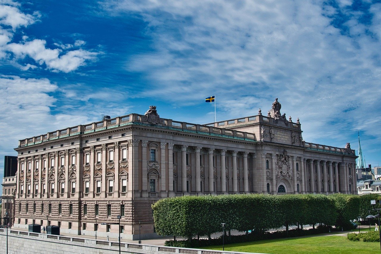 Historiska svenska kungliga slottet med detaljerad arkitektur och svensk flagga under en blå himmel med moln