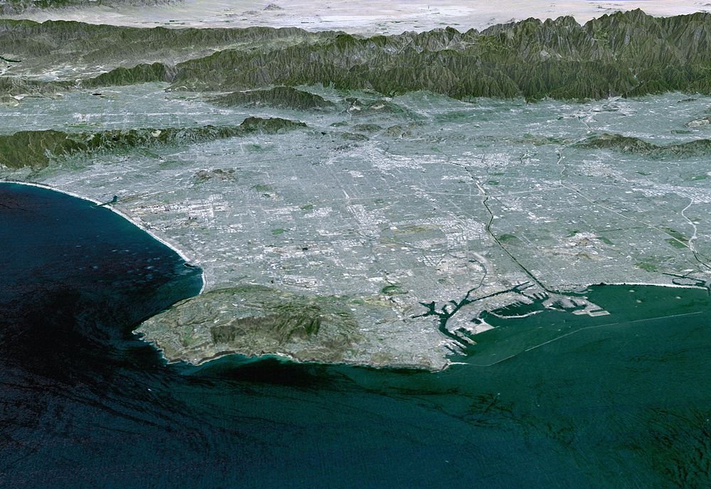 Flygfoto av kuststad med hamn och berg Flygfoto av en kuststad med berg i bakgrunden och ett stort hamnområde vid havet