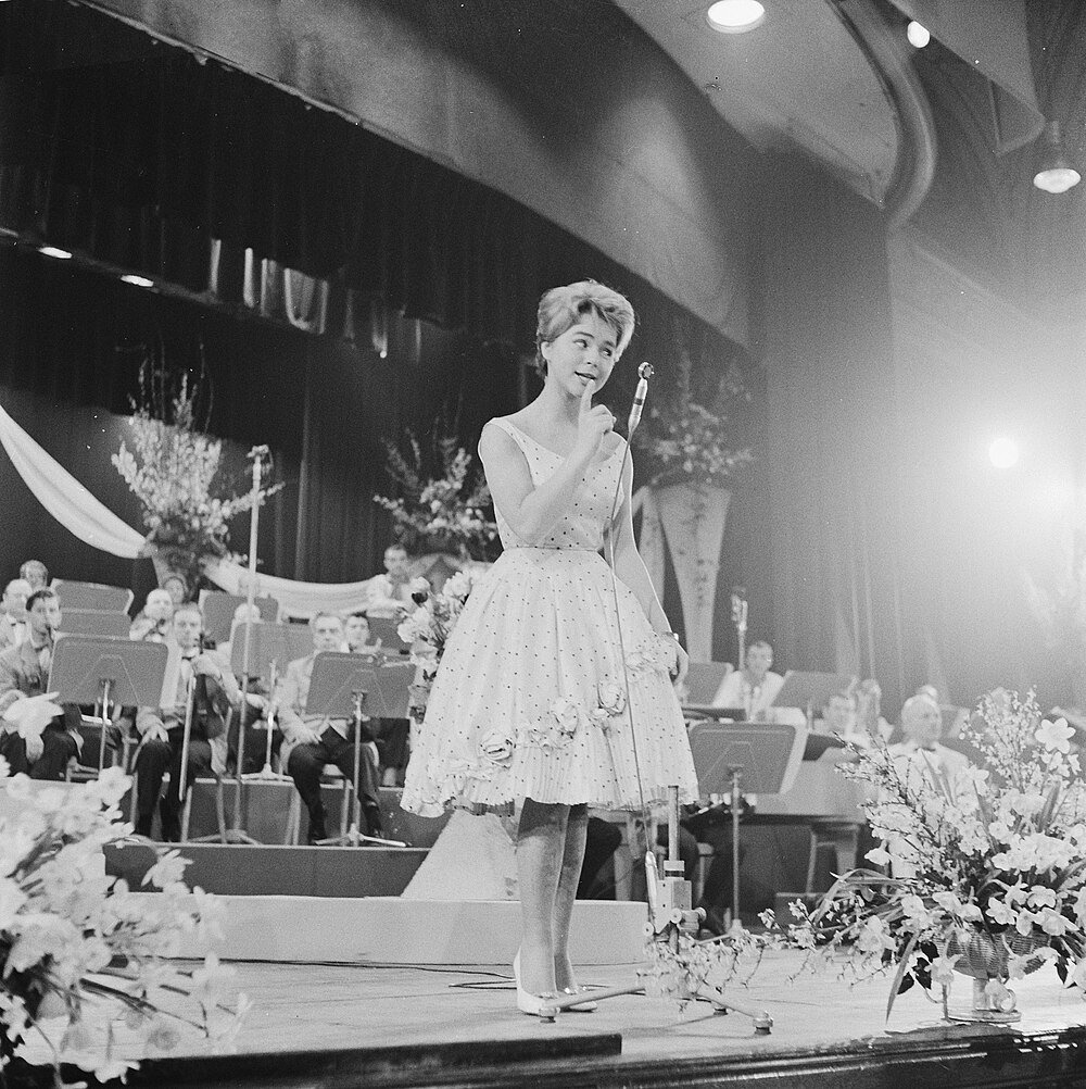 Ung kvinna sjunger på scen med orkester i bakgrunden under en vintagekonsert