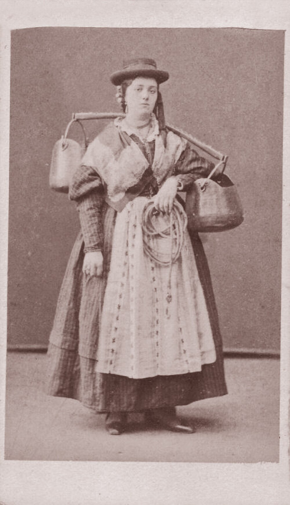 Vintage foto av kvinna med ok och behållare Vintage sepia foto av en kvinna i traditionell klädsel som bär två stora behållare med en ok