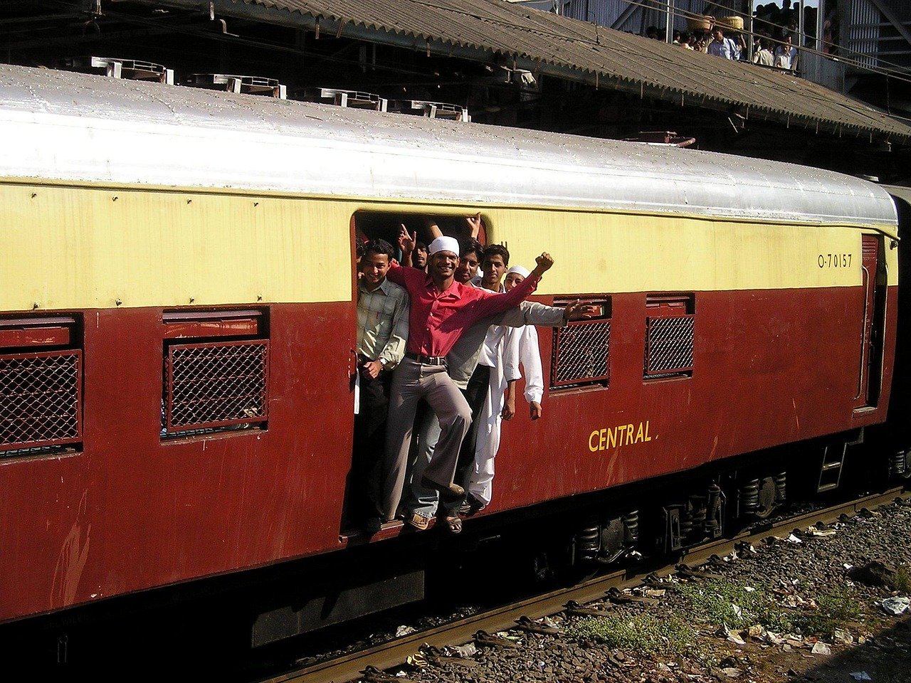 Grupp av unga män som hänger ut från ett rörligt tåg i Indien, visar upp spänning och traditionella kläder nära Central järnvägsstation.
