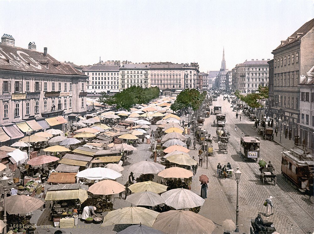 Historisk europeisk gatumarknad med spårvagnar och vagnar Historisk europeisk gatumarknad med färgglada paraplyer, hästdragna vagnar och vintage spårvagn i en livlig stadsscen