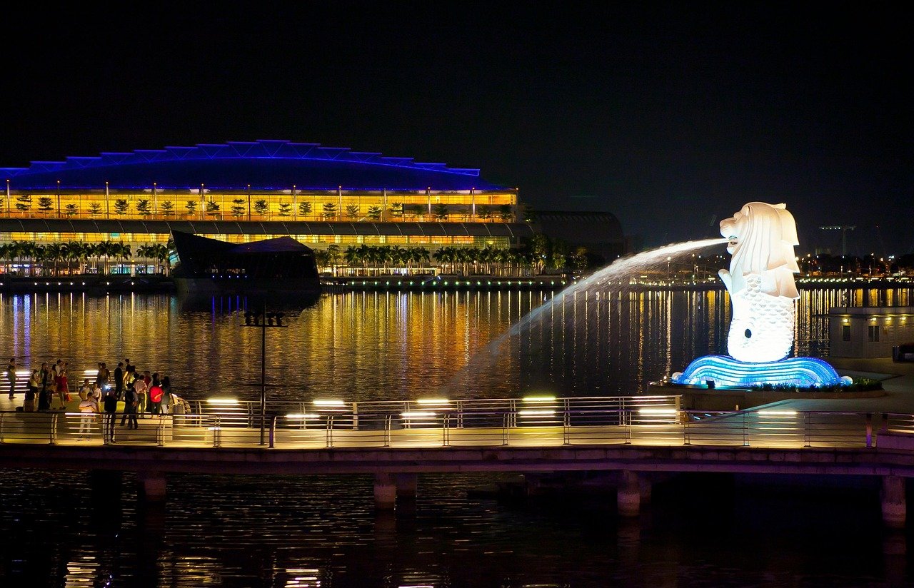 Nattvy av Singapore Merlion-staty med vattenfontän och upplysta strandbyggnader som reflekteras i vattnet