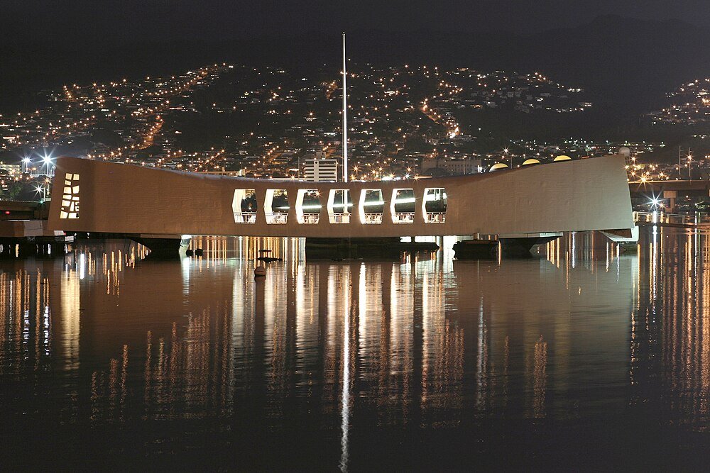 USS Arizona Memorial vid Pearl Harbor på natten Nattvy av USS Arizona Memorial vid Pearl Harbor med stadsljus som reflekteras på vattenytan